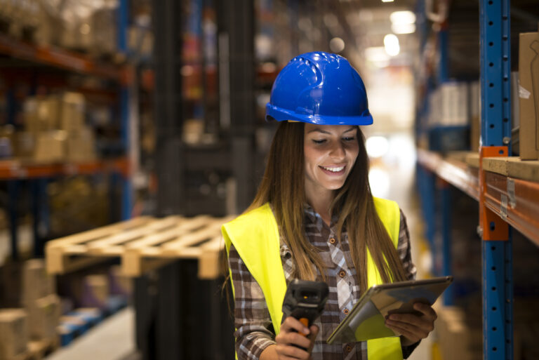 Woman worker holding tablet and bar code scanner checking inventory in large distribution warehouse.